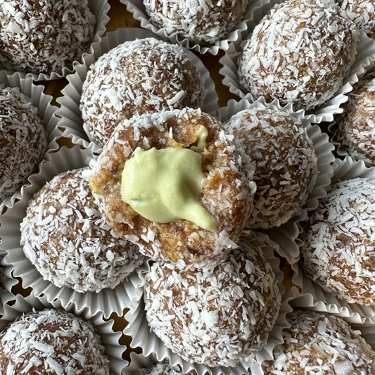 Image of several key lime pie energy balls, one is cut open revealing cream inside.